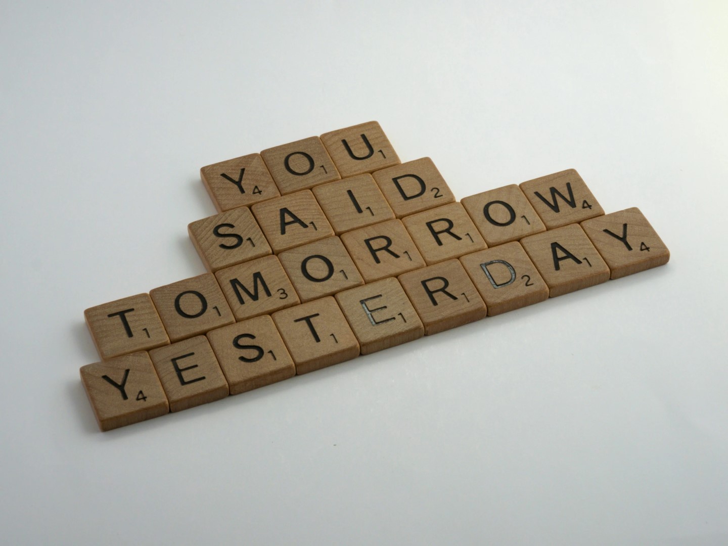 Układanka ze słów 'You said tomorrow yesterday' ułożona z drewnianych płytek do gry Scrabble na białym tle, przedstawiająca motywacyjne przesłanie