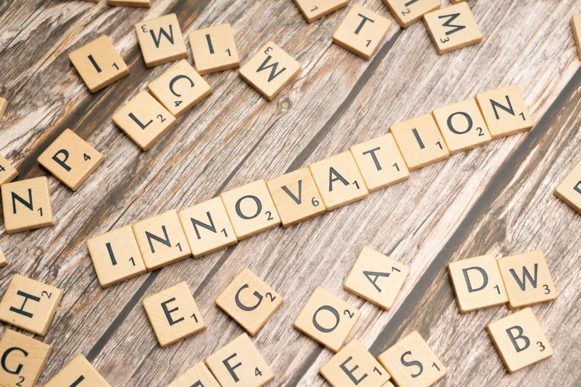 Drewniane płytki z literami układające się w słowo „innovation” na drewnianym tle.