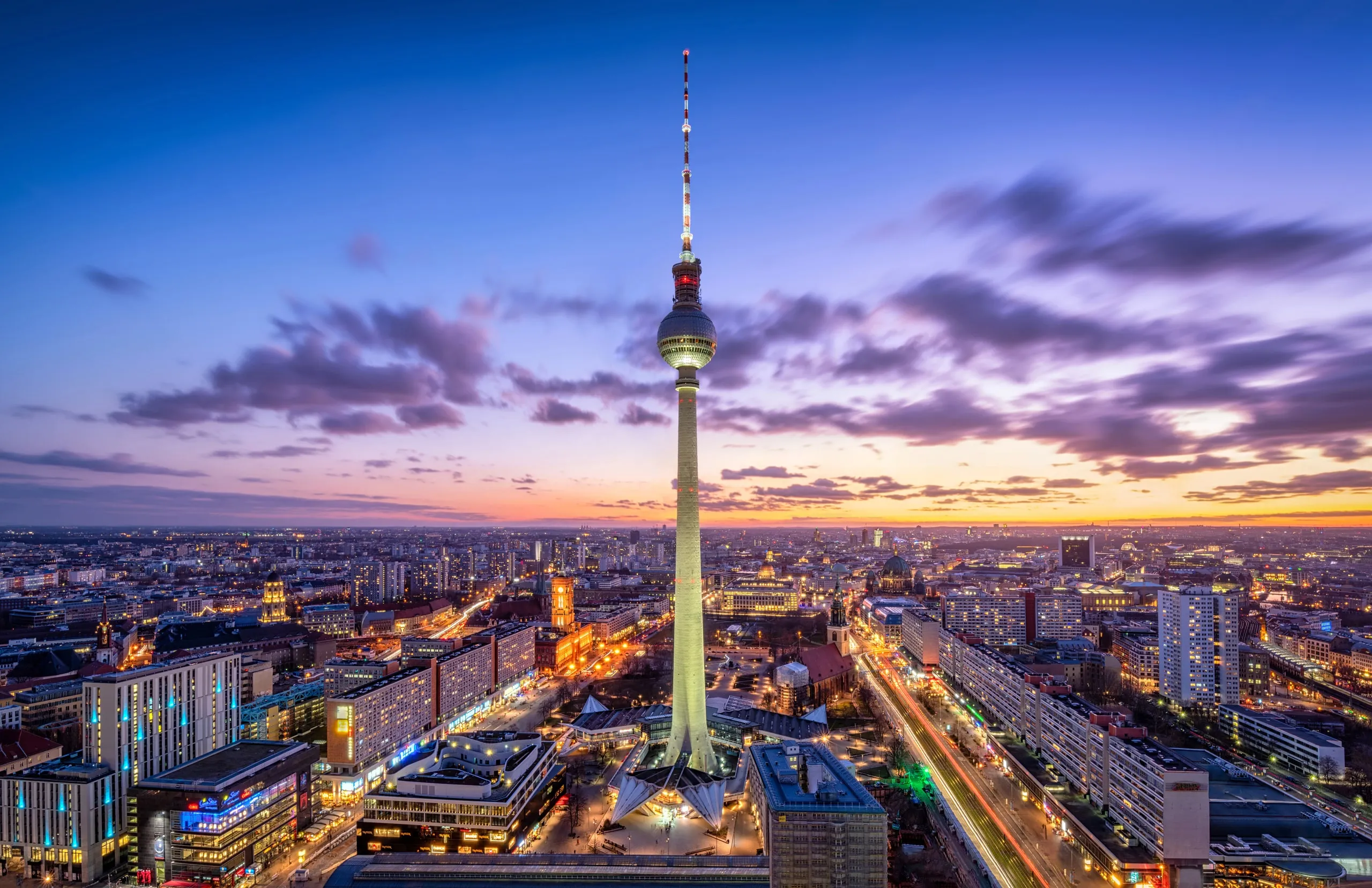 Panorama Berlina o zmierzchu z podświetloną wieżą telewizyjną, widok na miasto i ulice pełne świateł.
