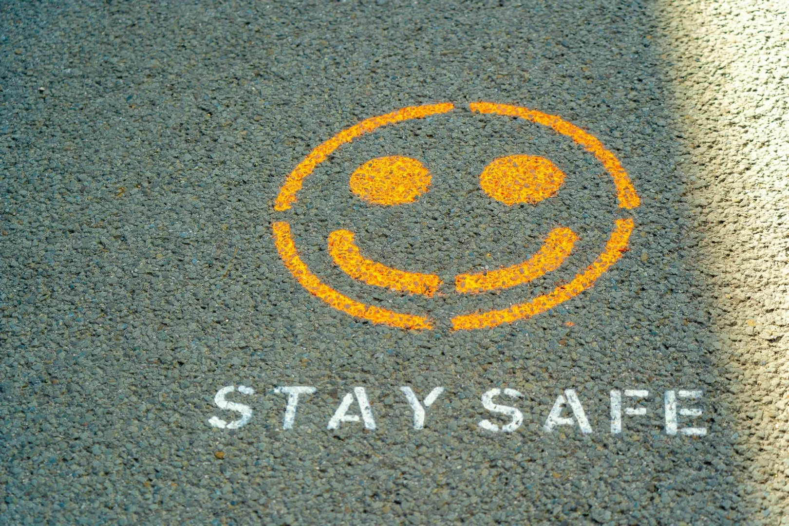 Napis "STAY SAFE" i uśmiechnięta buźka namalowane na asfalcie jako symbol szkolenia BHP dla studentów.